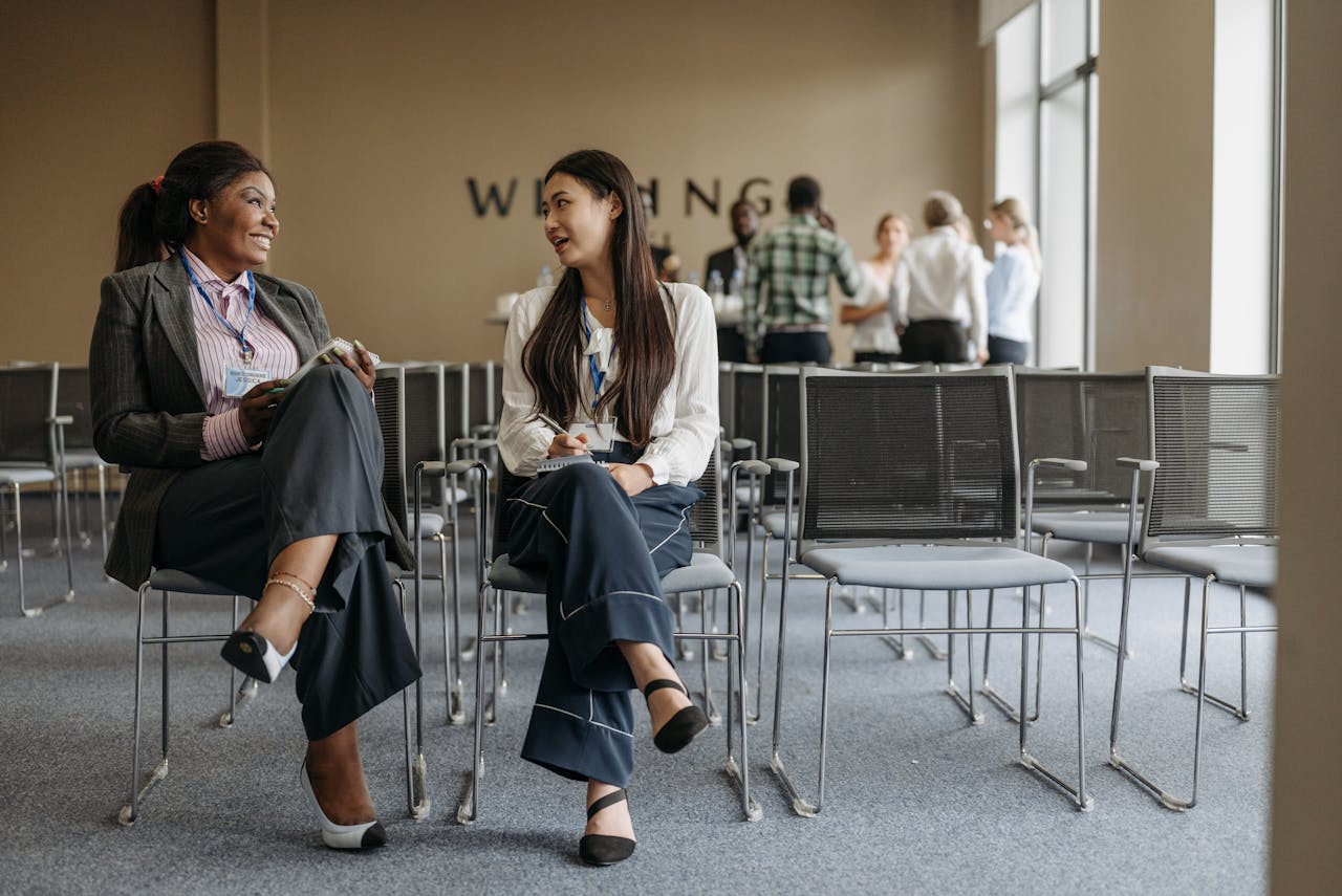 Two businesswomen talking during a conference break, showcasing teamwork.